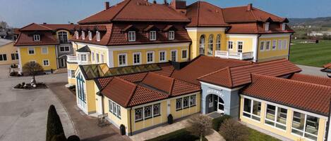 A large, multi-story building with a red-tiled roof, multiple windows, and a well-maintained lawn.