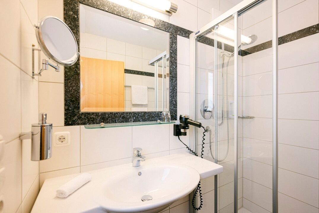 Un baño moderno con un lavamanos blanco, una cabina de ducha con paredes de vidrio y un espejo con un panel de madera encima.