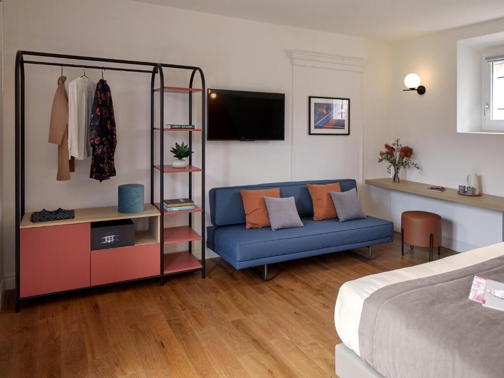 A modern bedroom with a bed, a blue sofa, a TV, a wardrobe, and a small table with a vase of flowers.