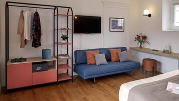 A modern bedroom with a bed, a blue sofa, a TV, a wardrobe, and a small table with a vase of flowers.
