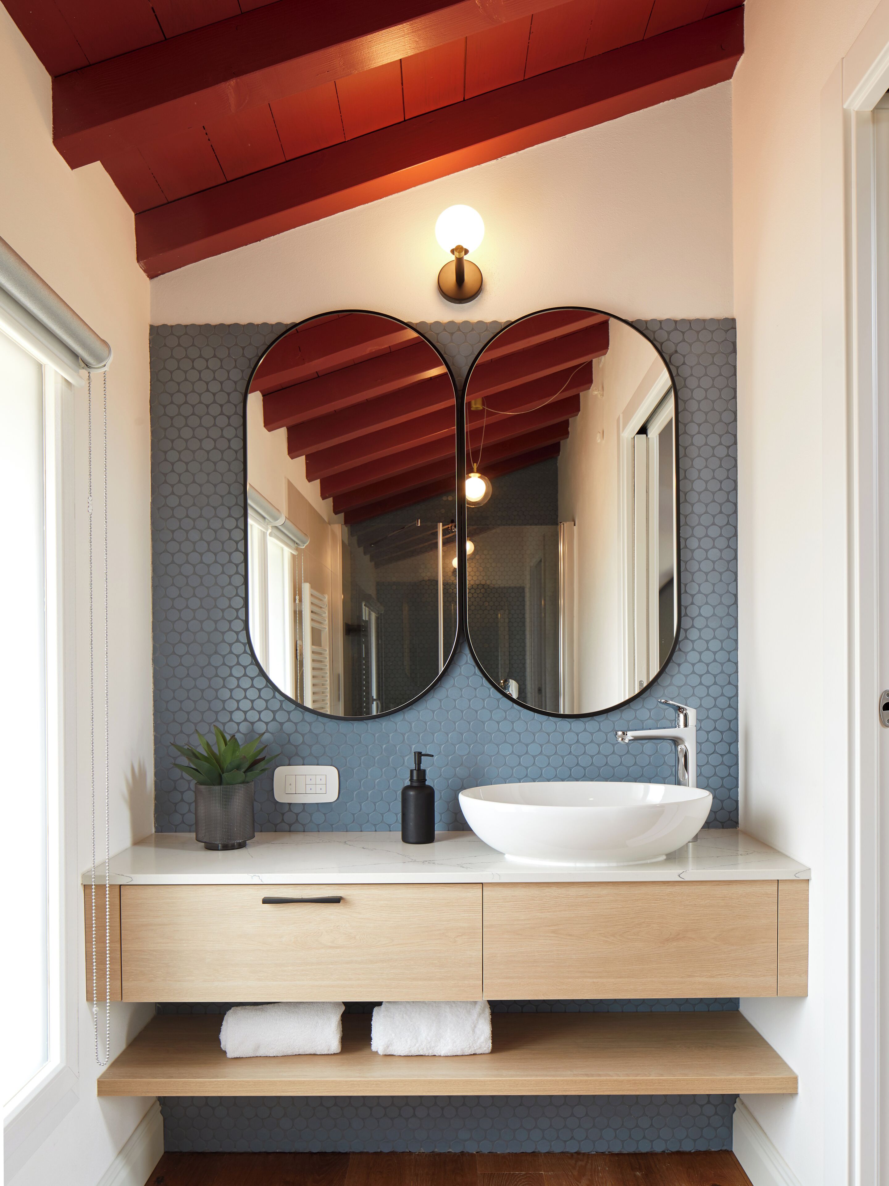 A bathroom with a white sink, two mirrors, a wooden vanity, and a red ceiling.