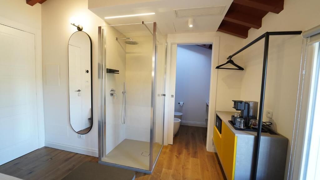 Un baño moderno con cabina de ducha de vidrio, un espejo y suelo de madera.