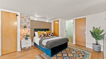 A bedroom with a bed, bedside tables, a patterned rug, and a potted plant.