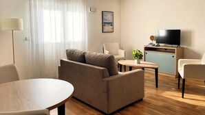 Een moderne woonkamer met een bank, een eettafel, een televisie en een kleine keukenhoek.