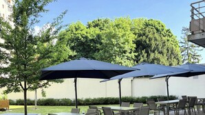 Een buitenterras met tafels en stoelen, overdekt met parasols, omringd door groen.