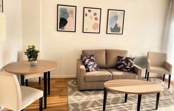 A modern living room with a sofa, two round tables, and a potted plant. - Zenao Appart'hôtels Orléans (Orléans)