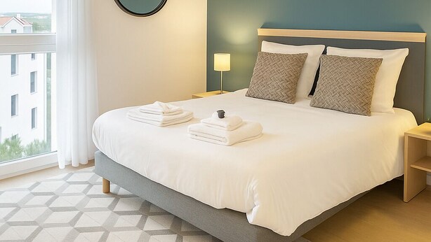 Een moderne hotelkamer met een groot bed, een ronde spiegel en uitzicht op gebouwen.