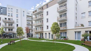Een modern appartementencomplex met meerdere balkons, een grasveld in het midden met banken, en een heldere lucht.