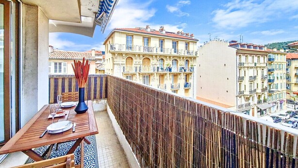 A balcony with a table set for dining, a view of the cityscape, and a bamboo fence. - N&J - TROPI AZUR - Terrace - Place du Pin  (Niza)