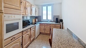 A kitchen with wooden cabinets, a built-in oven, a granite countertop, and a window providing natural light. - N&J - TROPI AZUR - Terrace - Place du Pin  (Niza)