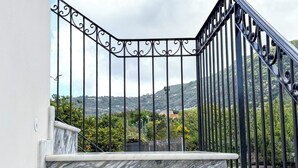 En marmortrappe med gelænder i sort jerngitter, der fører op til en balkon med et smukt udsigt over bakker og grønt.