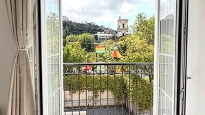 En balkon med fliset gulv og gelænder i metal, med udsigt over en gade med træer og bygninger.
