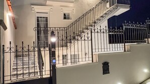 En bygning med flere etager, lys facade, balkon på øverste etage og en indgang med låge samt trappe til hovedindgangen.