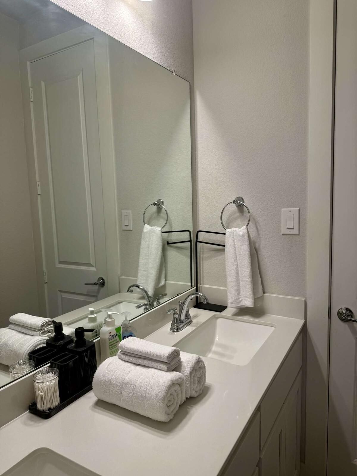 A bathroom with a large mirror, two sinks, and a towel rack.