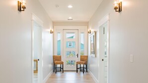A hallway with two wicker chairs, white walls, and a door with a window. - Family Beach House (Fort Myers Beach)