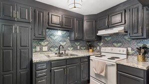 A kitchen with dark cabinets, a white stove, and a patterned backsplash. - The Raven's Roost Lake View Retreat 3bd 2ba (Rockaway Beach)