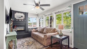 A cozy living room with a fireplace, a sofa, a coffee table, and a ceiling fan. - The Raven's Roost Lake View Retreat 3bd 2ba (Rockaway Beach)