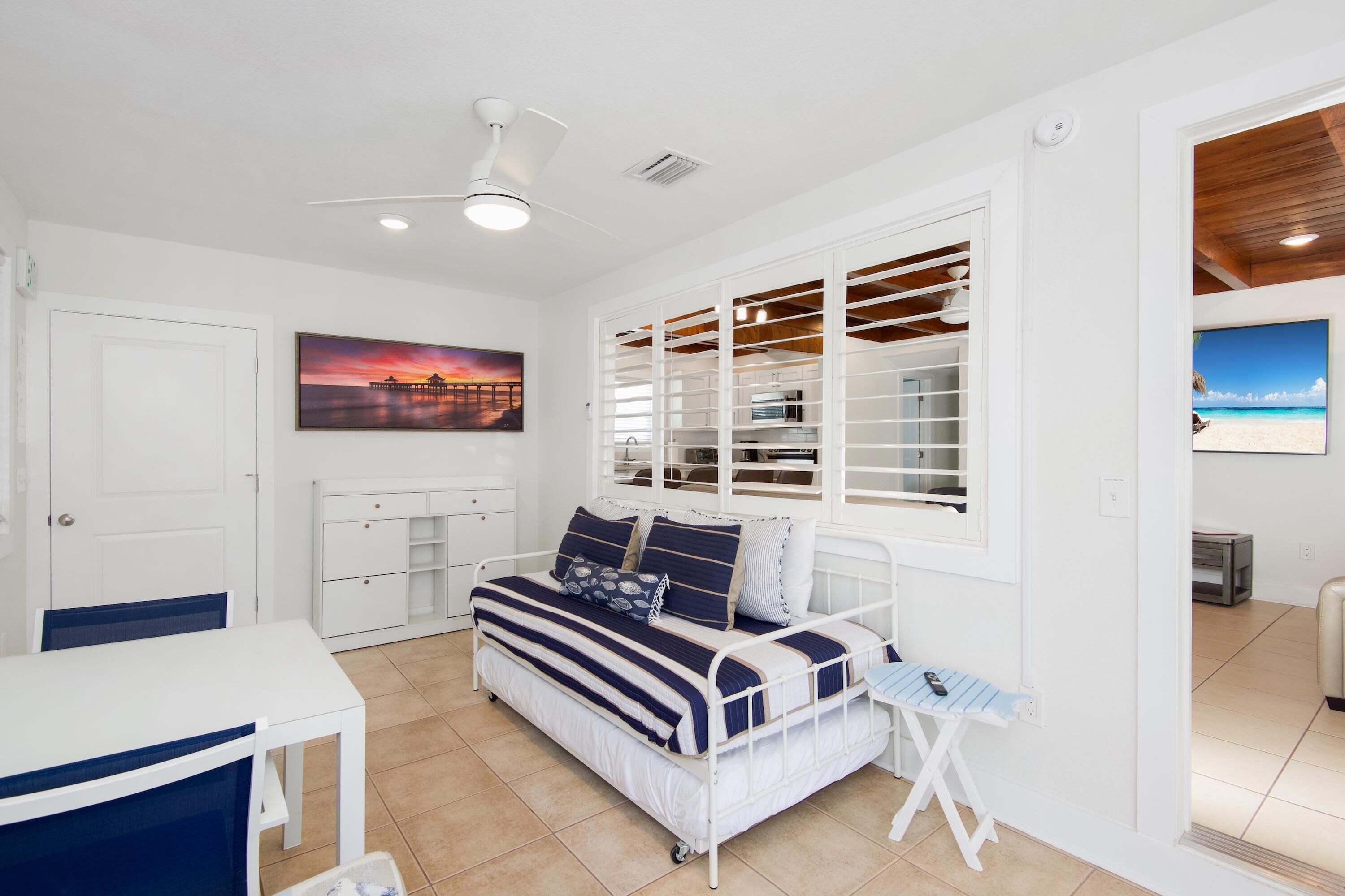 A bedroom with a bed, a desk, a chair, a window with blinds, and a ceiling fan.