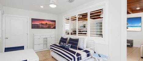A bedroom with a bed, a desk, a chair, a window with blinds, and a ceiling fan.