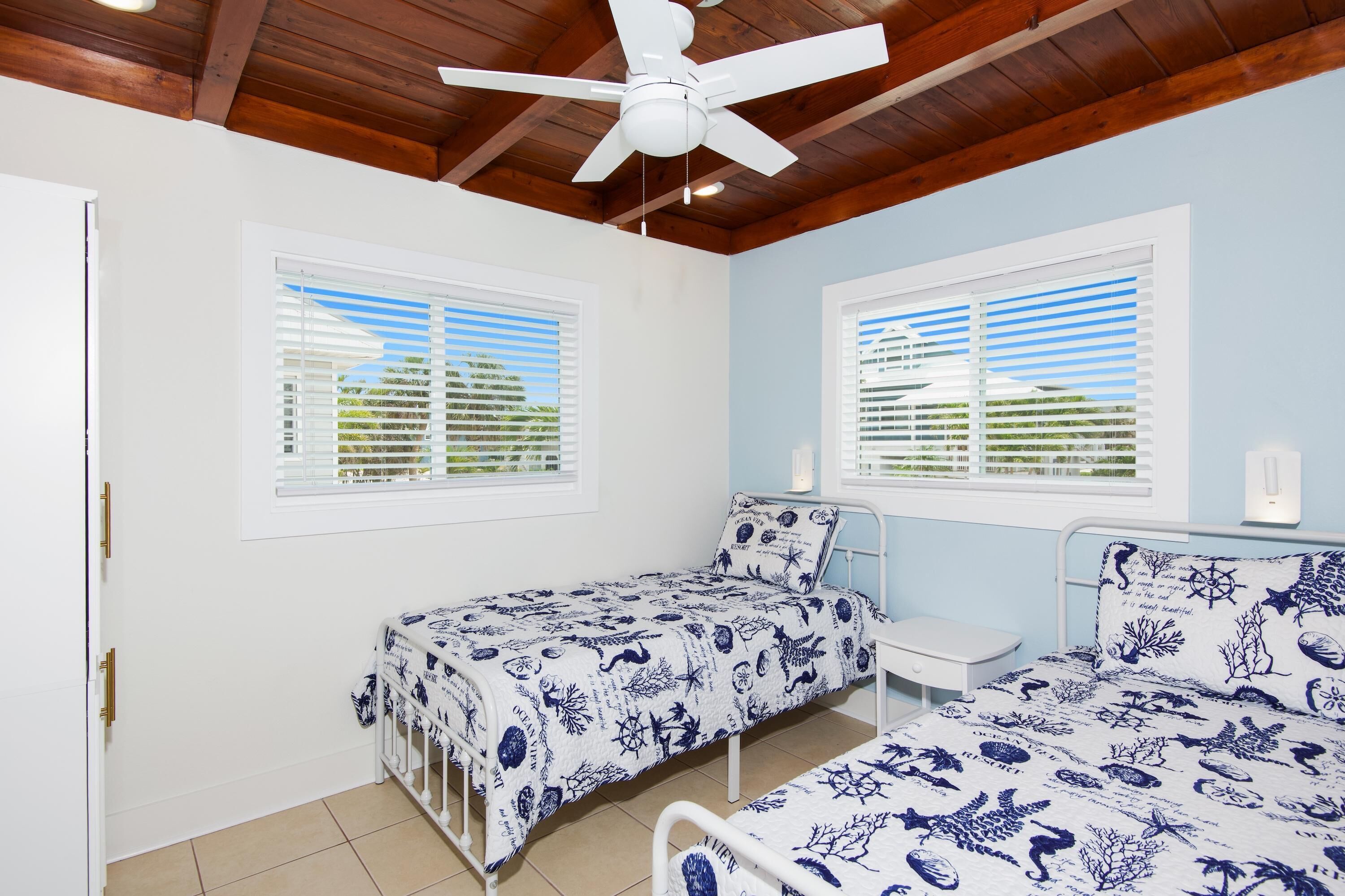 A bedroom with two single beds, a ceiling fan, and windows with blinds.