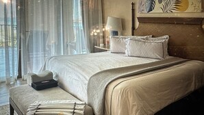 Ein ordentlich bezogenes Bett mit Kopfteil, ein Nachttisch mit Lampe und ein dekoratives Blattgemälde an der Wand.