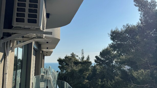 Un balcó amb barana de vidre que dona a una zona boscosa i un cos d'aigua.