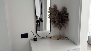 Un tocador blanc amb un mirall, un petit recipient negre amb un suport per bolígrafs i herba de pampa en un vas de vidre.
