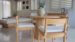 Ein modernes Wohnzimmer mit einem runden Holztisch, weißen Polsterstühlen und einem gewebten Korb mit Blumen.