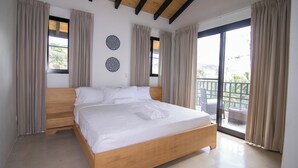 Ein Schlafzimmer mit einem Holzbett, beige farbenen Vorhängen und einem Balkon mit Korbmöbeln.