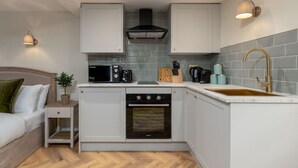 Una cocina compacta con gabinetes blancos, horno empotrado, microondas y un lavamanos con grifo dorado.