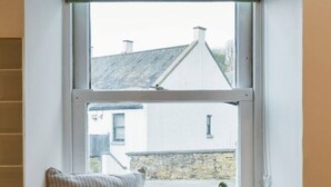 Asiento junto a la ventana con vista a una casa, un cojín verde y blanco a rayas, y un cojín a rayas.