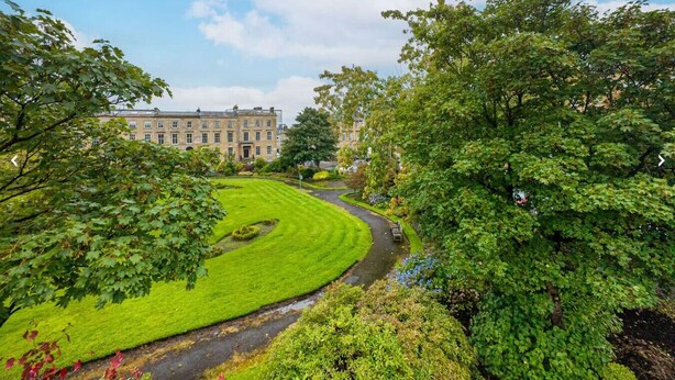 A landscaped garden with a curved pathway, a building in the background, and a clear sky.