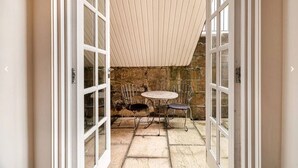 A stone patio with a round table and two chairs, leading to a stone wall and a wooden ceiling.