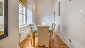 A dining area with a round table, six chairs, a window with blinds, a radiator, and a light fixture.