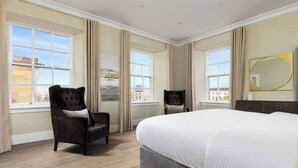 A hotel room with a large bed, two armchairs, a dresser, and large windows with curtains.