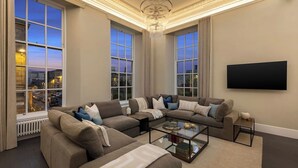 A modern living room with a sectional sofa, a glass coffee table, and a flat-screen TV mounted on the wall.
