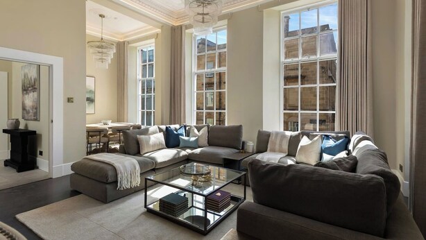 A spacious living room with a large sectional sofa, a glass coffee table, and a dining area with a table and chairs.