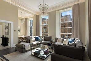 A spacious living room with a large sectional sofa, a glass coffee table, and a dining area with a table and chairs. - Luxury 4 Bedroom Apartment in Glasgow City Centre (Glasgow City)