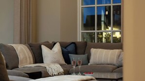 A cozy living room with a sectional sofa, a glass coffee table, and a view of the outdoors through a window.