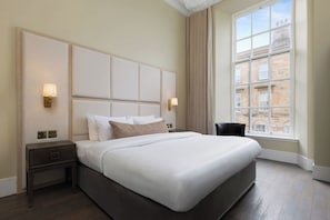 Une chambre d’hôtel avec un grand lit, une table de chevet, une chaise et une fenêtre donnant sur des immeubles.