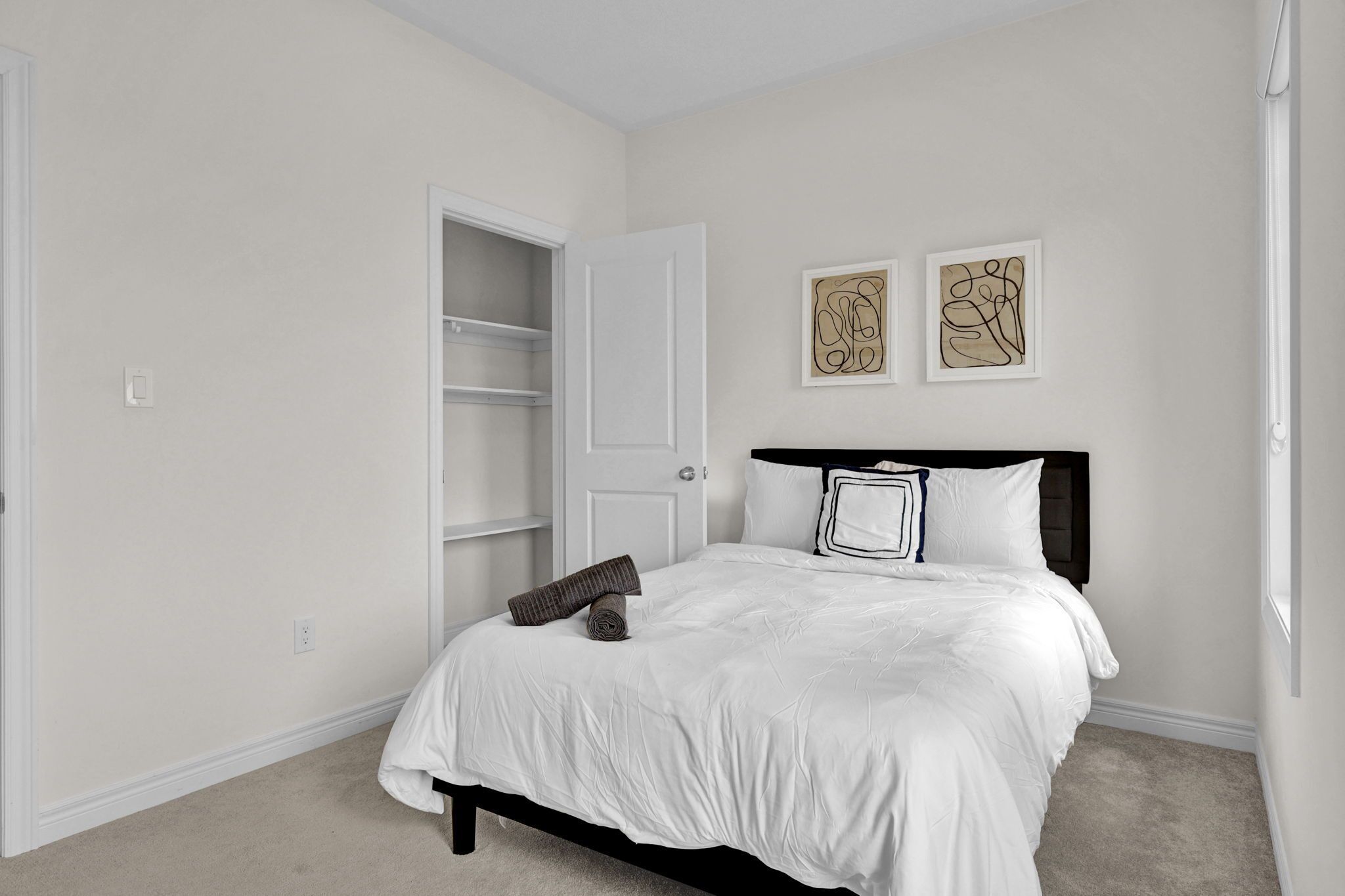 A bedroom with a bed, a door, and two framed artworks on the wall.