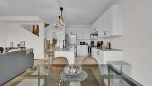 Una cocina moderna con armarios blancos, un refrigerador de acero inoxidable y una cafetera.