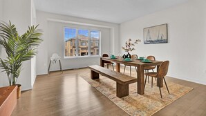 Un comedor con una mesa de madera, sillas y un banco. Se ve una ventana con vistas a edificios.