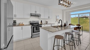 Una cocina moderna con armarios blancos, electrodomésticos de acero inoxidable, una isla grande con taburetes y vistas al exterior.