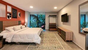 A modern bedroom with a large bed, a wooden bench, a TV, and a view of greenery outside.