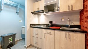 A compact kitchen with light wood cabinets, a stainless steel microwave, a gas stove, and a sink.