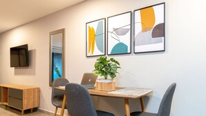 A modern dining area with a wooden table, grey upholstered chairs, a potted plant, and abstract wall art.