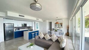 A modern living room with a grey sofa, white coffee table, and a dining area with a blue table and white chairs. - Apartamento Vista Mare 9.102 (Samana)