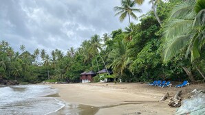 A beach with palm trees, a small wooden structure, and blue lounge chairs. - Apartamento Vista Mare 9.102 (Samana)