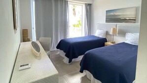 A hotel room with two beds, a desk with a mirror, a window with curtains, and a painting on the wall. - Apartamento Vista Mare 9.102 (Samana)